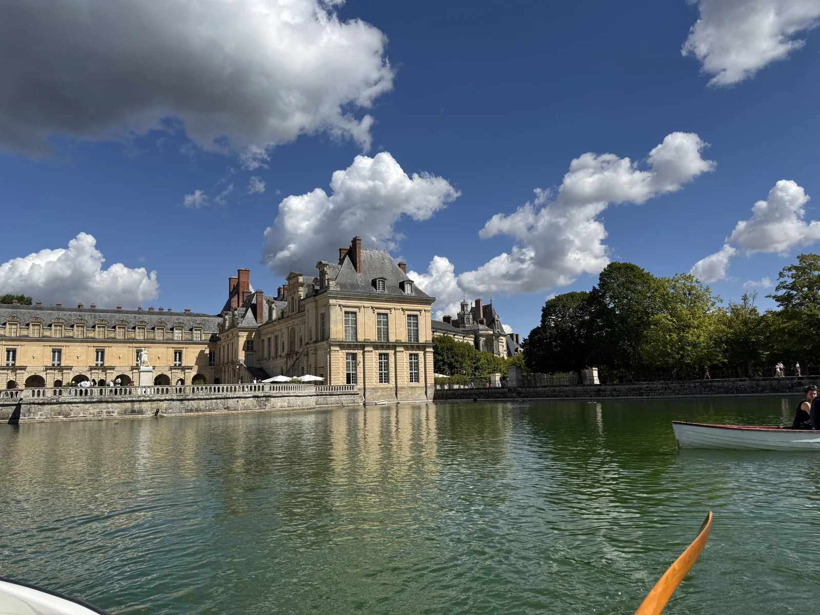 Château de Fontainebleau and its pond seen from a boat, with a rowing boat on the water under a blue sky